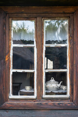 A weathered wooden window frames a cozy scene: a classic porcelain teapot and matching cups sit on a lace-draped table