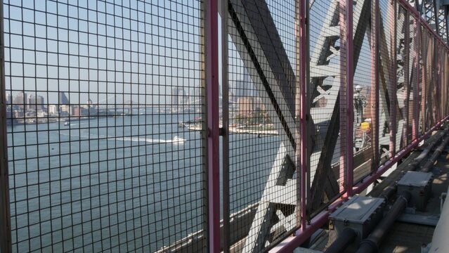 Williamsburg Bridge in Brooklyn, New York City, United States. Transport metallic bridge near Marcy Av subway station and Domino park in Williamsburg. East River and Manhattan view thru pink fence.