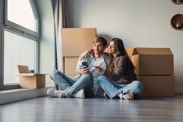 A dreamy couple rests in their new apartment among packed boxes, looking away thoughtfully while planning decoration ideas and envisioning their future home © Daniel