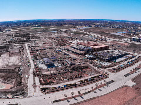 Aerial view of construction site teeming with activity under a vast blue sky, a stark contrast to the raw earth and steel framework, Frisco, Texas, United States.