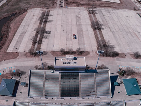 Aerial view of a stadium under the winter sun, where bare trees cast long shadows across the vast parking lot, Denton, Texas, United States.