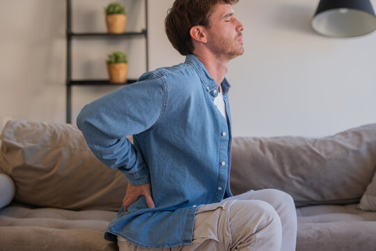 Upset tired young man feeling pain massaging stiff back rubbing tensed muscles to relieve back ache joint shoulder discomfort after long sedentary work in incorrect posture, fibromyalgia concept
