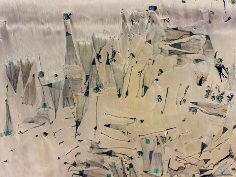 Aerial view of fishing nets cast shadows on the sandy beach, creating a textured tapestry of light and shade, Cox's Bazar, Chittagong Division, Bangladesh.