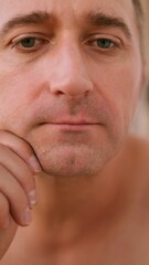 Naklejka premium Vertical photo Caucasian man reviews facial hair closely, Man from Caucasian background diligently assesses skin and beard condition, Individual of Caucasian ethnicity thoroughly inspects facial skin