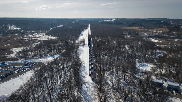 Aerial view of a long line of train cars cutting through the snowy landscape, woods and open spaces, Framingham, Massachusetts, United States.