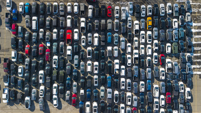 Aerial view of tightly parked cars, a metallic ocean reflecting sunlight, with pops of red, yellow, and blue adding vibrancy to the scene, Framingham, Massachusetts, United States.