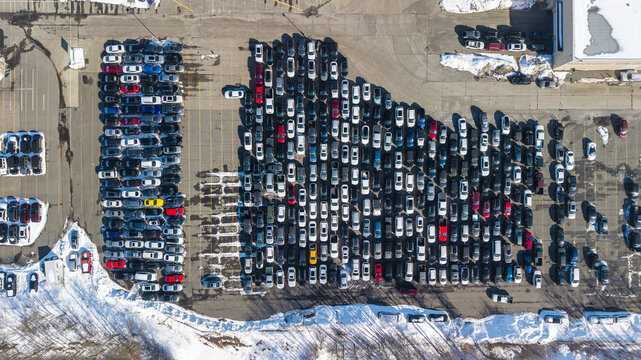 Aerial view of rows of parked cars glinting under the winter sun, creating a mosaic of color against the muted snow and asphalt, Framingham, Massachusetts, United States.