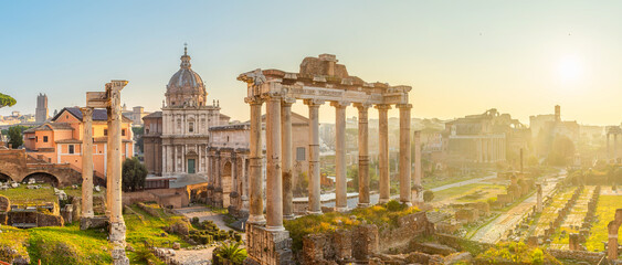 Naklejka premium Panoramic view of Roman Forum at sunrise in Rome city, Italy. Ancient temple columns and ruins, historic churches and archaeological remains. Italian architecture. Popular touristic landmark