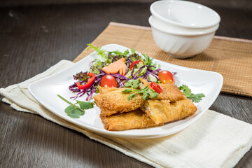A white plate with golden fried spring rolls served alongside fresh salad greens and tomatoes.