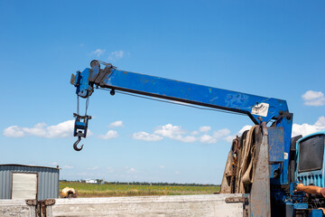 A blue mobile crane arm with a hook is positioned over a truck and construction site. industrial equipment, construction machinery, cargo loading. © Natalia