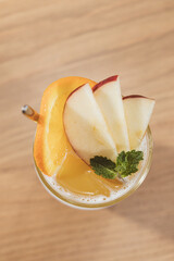 A glass of fresh fruit juice topped with orange and apple slices and a mint leaf garnish. © Phototora
