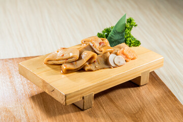 A wooden board with marinated pig ears arranged neatly and garnished with chili and herbs. © Phototora