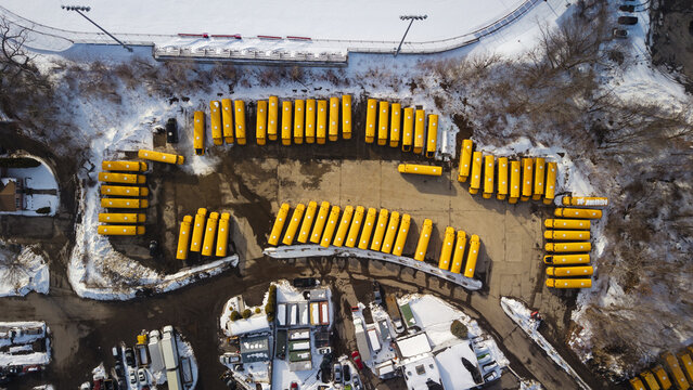 Aerial view of yellow school buses nestled in a depot near a snow-dusted field, creating a vibrant contrast against the winter landscape, Providence, Rhode Island, United States.