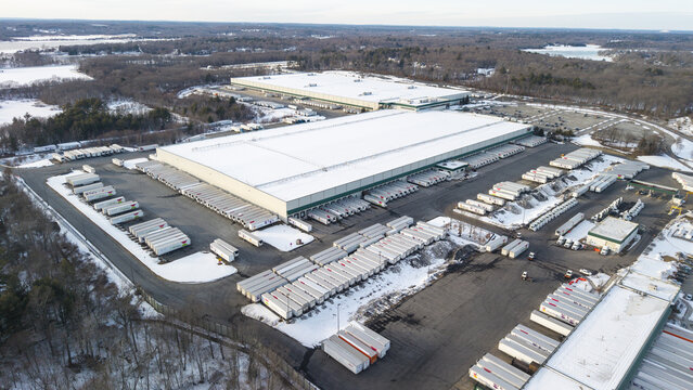Aerial view of a sprawling industrial landscape where snow-dusted warehouses meet orderly rows of trailers under a pale winter sky, Fall River, Massachusetts, United States.