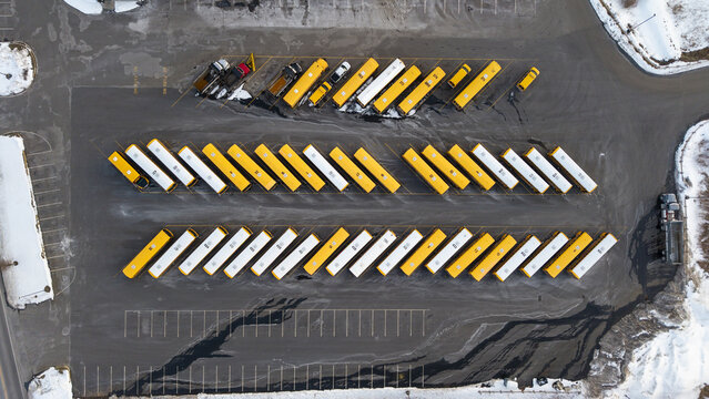 Aerial view of rows of yellow and white school buses parked neatly in a lot, creating a striking geometric pattern against the asphalt, Fall River, Massachusetts, United States.