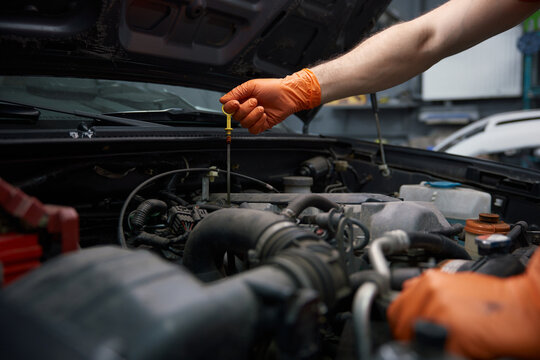 A mechanic checks engine oil with gloves in a garage