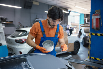 Technician is meticulously prepping a car panel with primer in a garage workshop