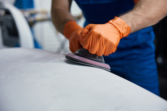 Worker sanding car surface with orbital sander - orange gloves in auto body workshop detail