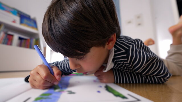Young boy lying on the floor, drawing with a blue marker, deeply immersed in creative activity, focused expression, engaged in artistic learning and imagination at home