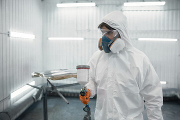 A worker dressed in a protective suit is spray-painting a car panel inside a modern paint booth