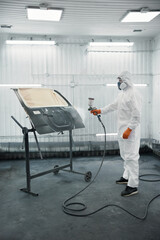An automotive technician is spray-painting a car panel in a protective paint booth