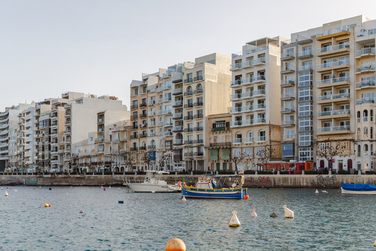 View of the calm waters reflecting the warm glow of the buildings and boats gently bobbing near the shore, St. Julian's, Malta.