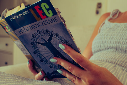 Warsaw, Poland - August 11, 2025: A woman holds and reads a worn copy of Myśli nieuczesane by Stanisław Jerzy Lec, marked with numerous tabs and notes