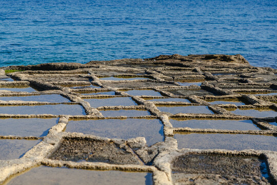 View of the ancient salt pans reflecting the azure sky above the rocky coastline, a testament to time and tradition, Marsaskala, Malta.