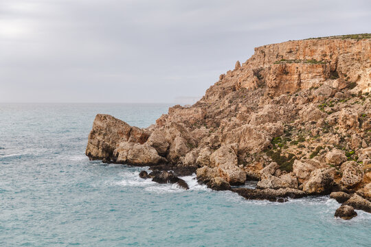 View of rugged, sun-kissed cliffs meet the turquoise sea under a serene sky, a dance of light and shadow on the Maltese coast, Il-Mellieha, Malta.
