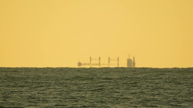 Mirage ship horizon appears as a fata morgana silhouette on the golden sea during a hazy sunset creating a mysterious atmosphere