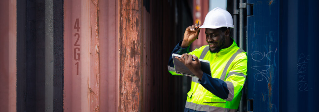African logistics supervisor using tablet to inspect shipping containers at port yard, managing cargo, safety, and supply chain operations in global transportation industry.