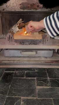 Hand placing birch bark kindling and lighting fire in indoor fireplace insert, starting wood burning flame for home heating