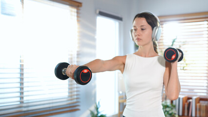 Athletic woman lifting dumbbells and listening to music with headphones during home workout