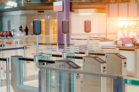 Automated e-gates with electronic screens are open for passenger entry at a modern airport terminal during daytime. Queue barriers guide travelers through security checks