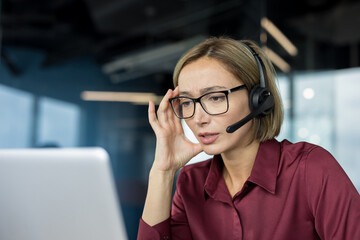 Stressed woman call center agent having a severe headache and looking tired while working on her laptop in a modern office, depicting job burnout and pressure