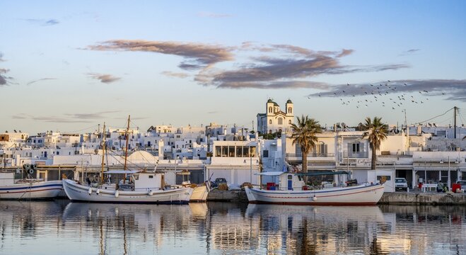 View of Naoussa, Fishing boats in the harbour at sunset, reflected in the sea, White Cycladic houses and church Agios Faneromeni, Naoussa, Paros, Cyclades, Greece