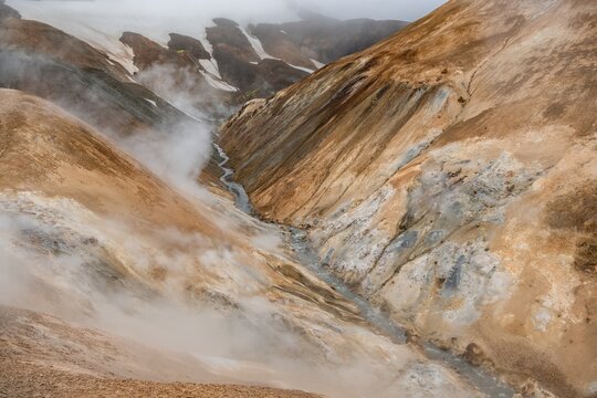 Steaming stream between colourful rhyolite mountains and snowfields, Hveradalir geothermal area, Kerlingarfj&ouml;ll, Icelandic Highlands, Iceland