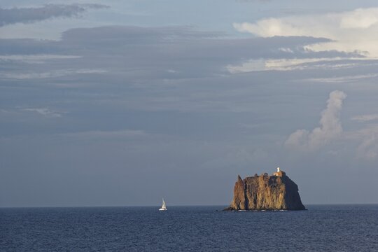Sailboat in front of the small island of Eolie with lighthouse, San Vincenzo, Stromboli at sunset, Stromboli, Calabria, Italy
