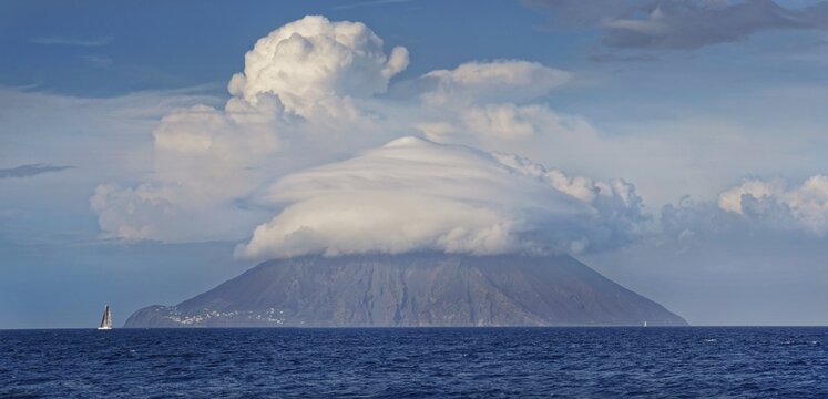 Sailing ship in front of Stromboli volcano and island with bizarre cloudscape, Stromboli, Calabria, Italy
