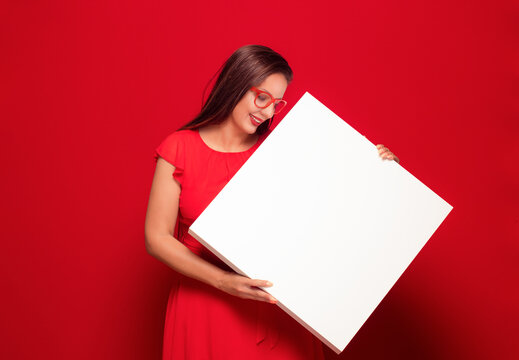 Promoter women holding white board, isolated on red background. Pretty girl showing blank empty paper billboard with blank space for text.