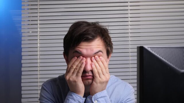 Overworked office worker rubbing his eyes from screen fatigue and eye strain after long hours at the computer, showing stress, drowsiness and need for a break from work