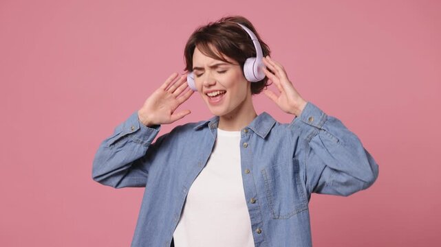 Vivid cheerful young woman wearing blue shirt white t-shirt casual clothes listen mp3 music in headphones dance sing song fooling around have fun enjoy relax isolated on plain pastel pink background