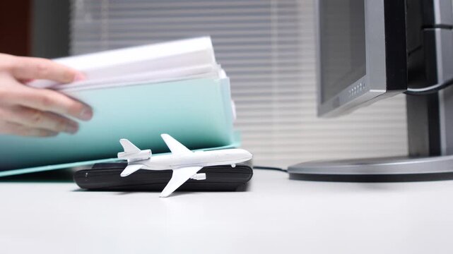 Hand placing documents in a folder on a desk with a model airplane, symbolizing aspirations for vacations or business trips potentially interrupting work