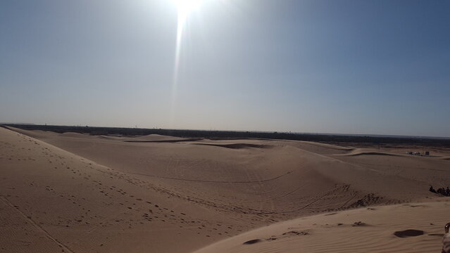 Sandy dunes stretch across the desert landscape under a bright sunny sky with clear blue atmosphere from a high vantage viewpoint