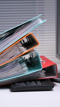 Vertical video stacked office binders overflowing with documents on a crowded desk, symbolizing bureaucratic overload and data chaos