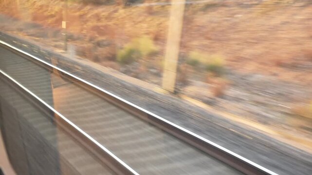 A train is traveling down the tracks with a beautiful landscape in the background. The train is moving quickly, and the landscape is blurred, giving the impression of motion. The scene is peaceful