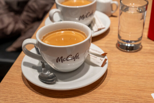 Vienna, Austria- Feb 21, 2026: Close-up view of two cups of McCafe coffee on a wooden table with sugar and a glass of water in a cozy cafe setting.
