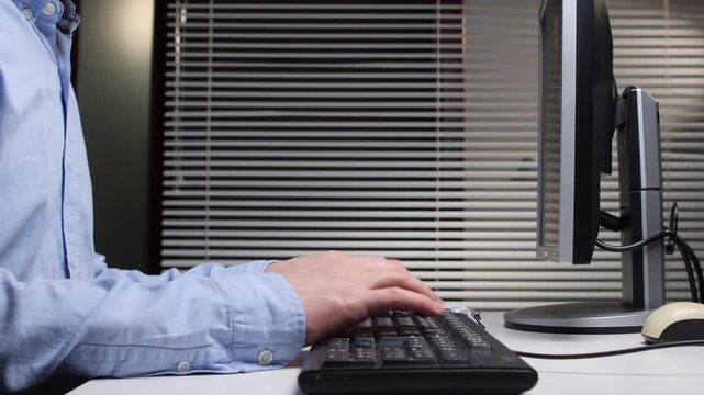 Hands of a professional person typing on a black computer keyboard, working at an office desk with a monitor and a mouse, demonstrating data entry and digital communication