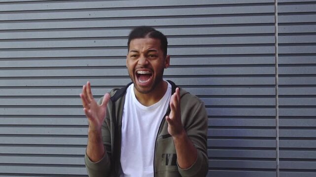 African American man in stress screaming and covering his ears outdoors, angry guy showing emotions of frustration and panic against wall background