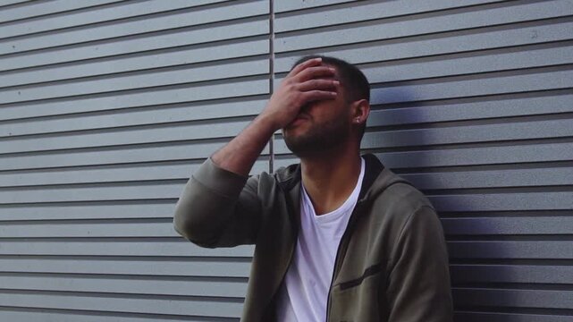 African American man suffers from mistake and regrets outdoors, unhappy guy shows facepalm from failure and burnout against wall
